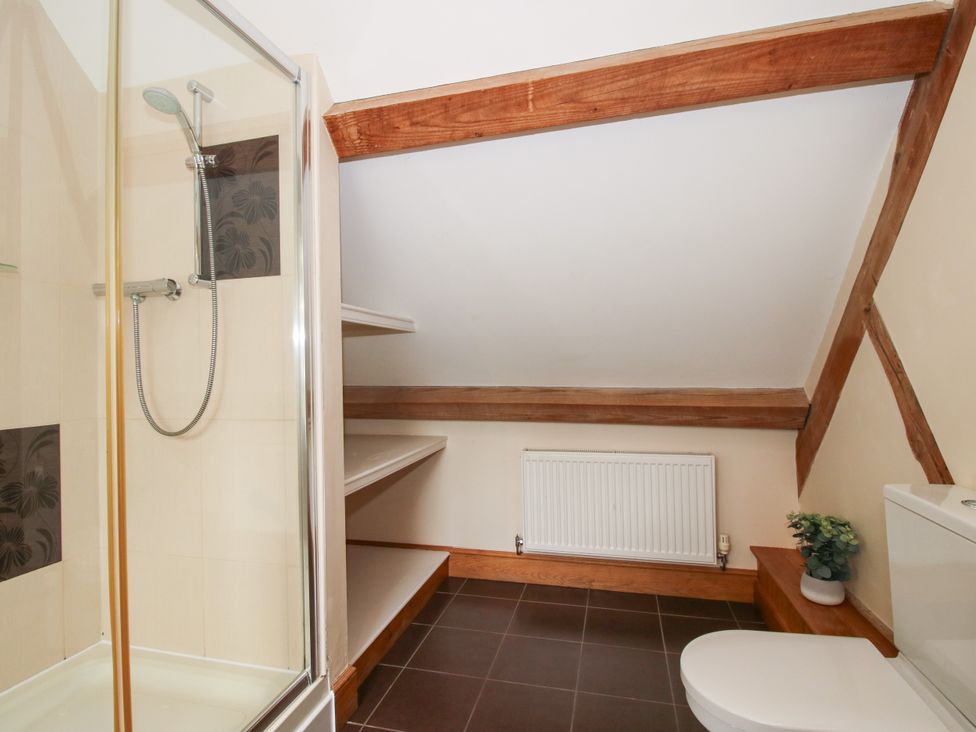 A bathroom with a shower, toilet, radiator, and shelves at The Olde Cowshed in Westhope near Church Stretton