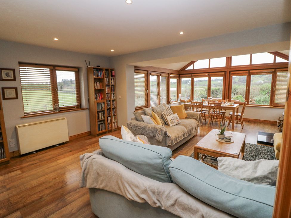 A living room with a bookshelf and large windows at Lough Cluhir Cottage in Union Hall, County Cork