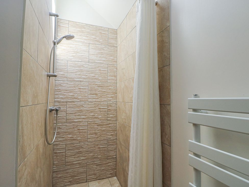 A shower area with tiled walls and a shower head at Lily Cottage in Caeathro near Caernarfon