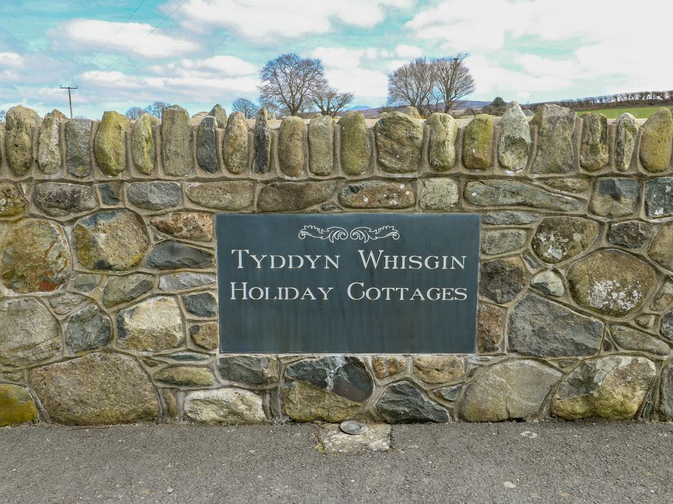 A sign for Tyddyn Whisgin Holiday Cottages on a stone wall in Caeathro near Caernarfon