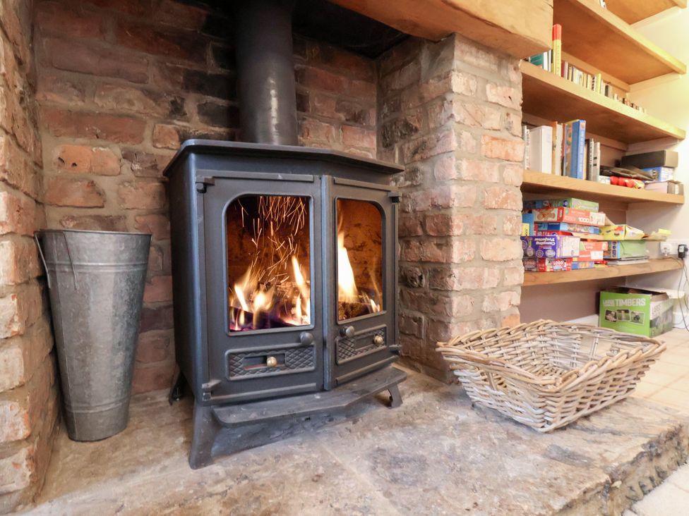 A wood stove with a fire in front of shelves and a basket at The Lodge Snainton near Scarborough
