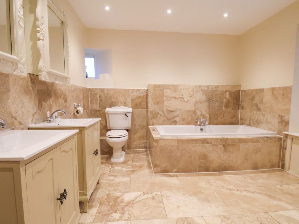 A bathroom with a bathtub, sink, toilet, and mirrors at The Lodge in Snainton near Scarborough