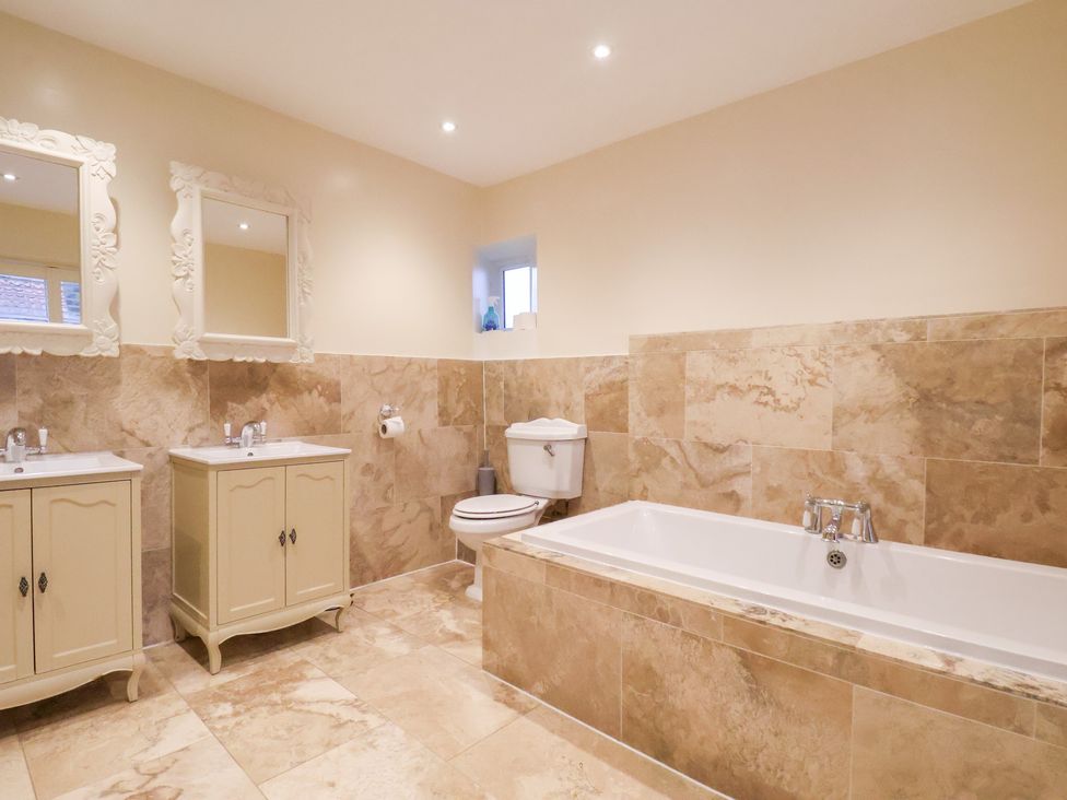 A bathroom with a bathtub, sink, toilet, and mirrors at The Lodge in Snainton near Scarborough