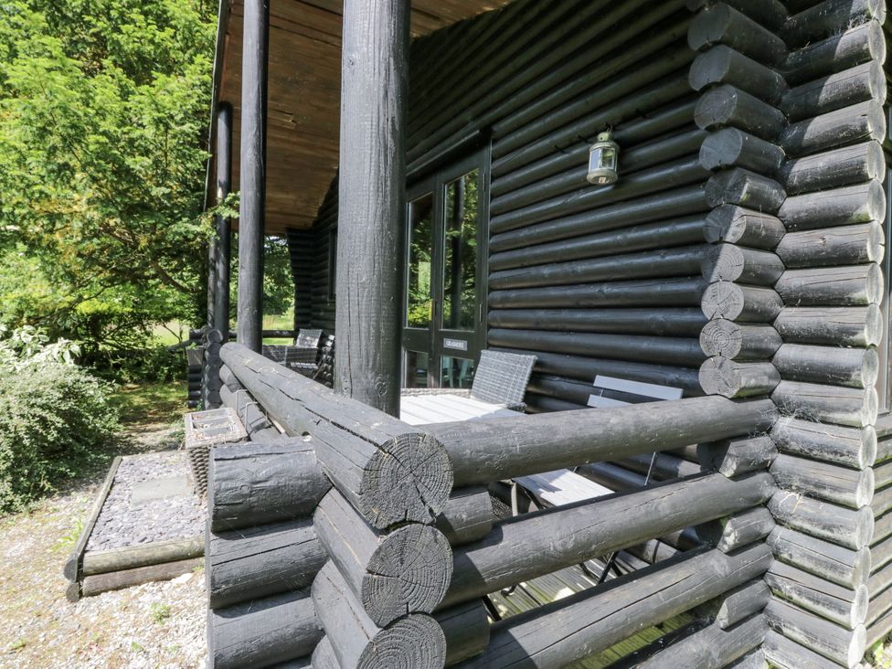 A log cabin porch with seating and a lantern at Grasmere Spark Bridge near Greenodd