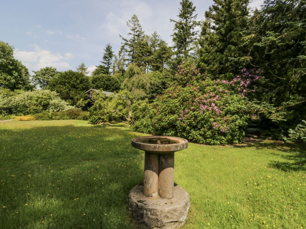 A garden with a birdbath and surrounding trees and flowering bushes at Grasmere in Spark Bridge near Greenodd