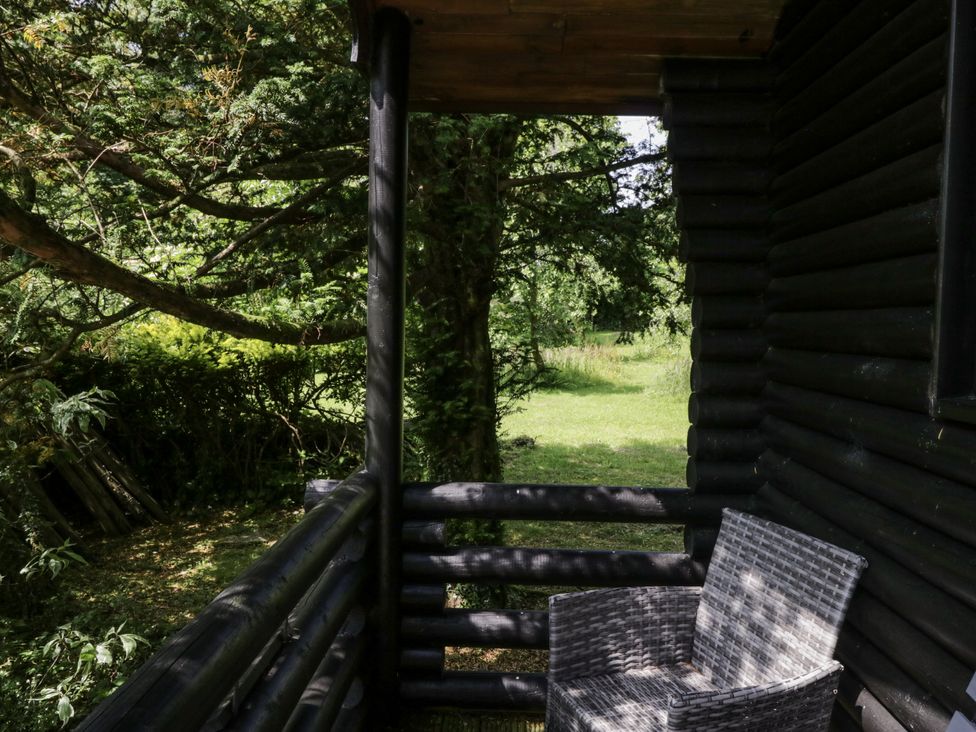 A chair on a balcony with trees and grass at Grasmere in Spark Bridge near Greenodd