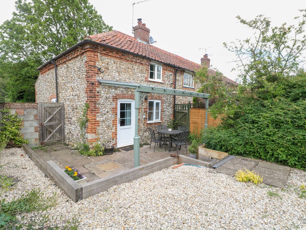 A garden with a stone house and seating area at Broom Cottage in East Rudham near Fakenham