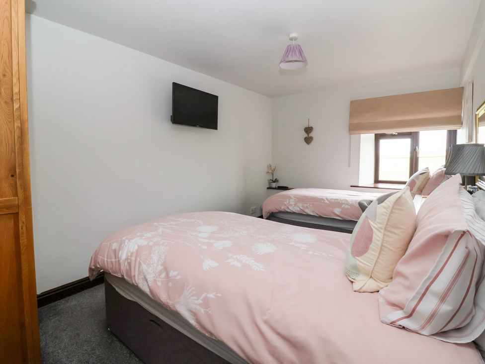 A bedroom with two beds and a television mounted on the wall at Wethercote Cottage Old Byland near Helmsley