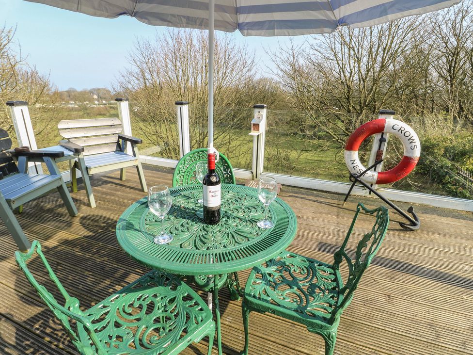 A table with chairs and a wine bottle under an umbrella at Crow's Nest Cottage Tynygongl near Benllech