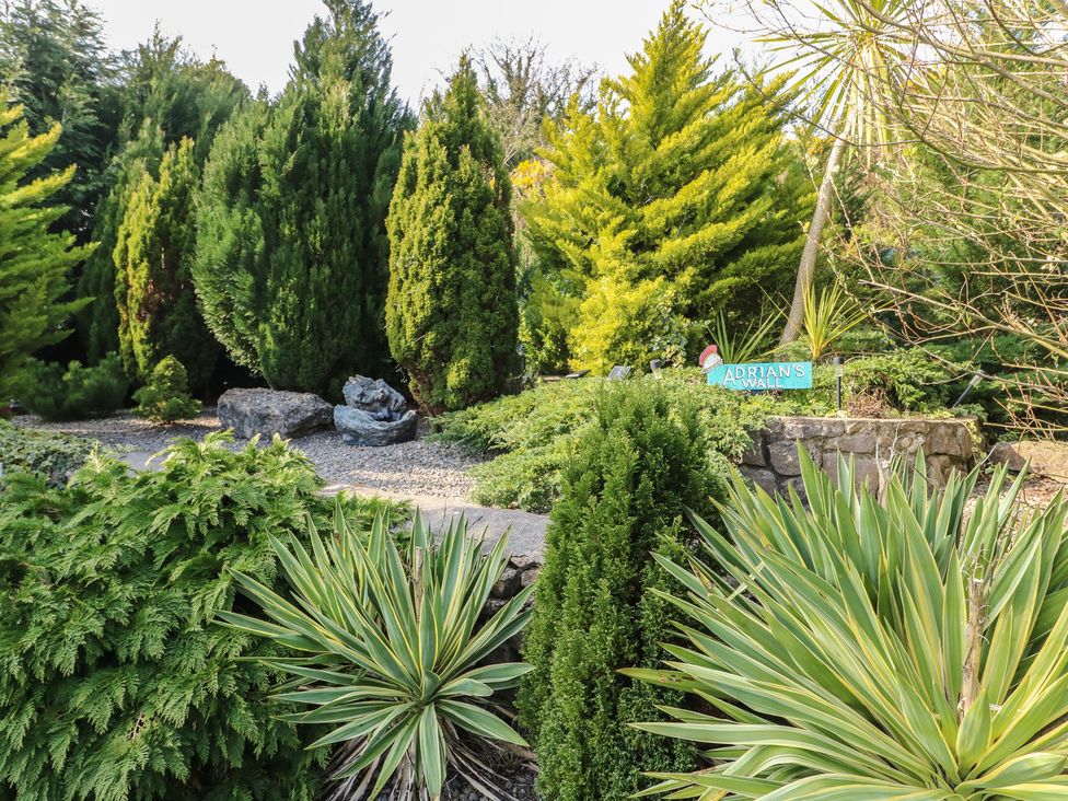 A garden with various trees and a sign at Crow's Nest Cottage in Tynygongl near Benllech
