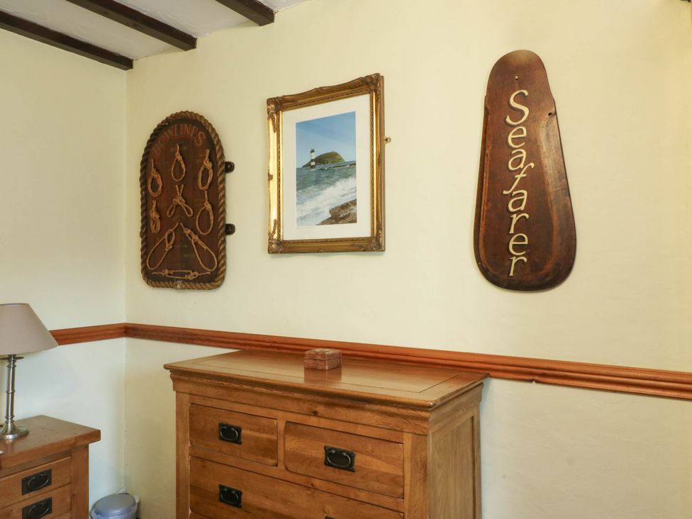 A wall with a wooden sign and a framed picture at Crow's Nest Cottage in Tynygongl near Benllech