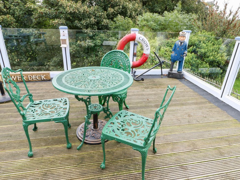 A table and chairs on a deck with a life buoy and statue at Crow's Nest Cottage in Tynygongl near Benllech