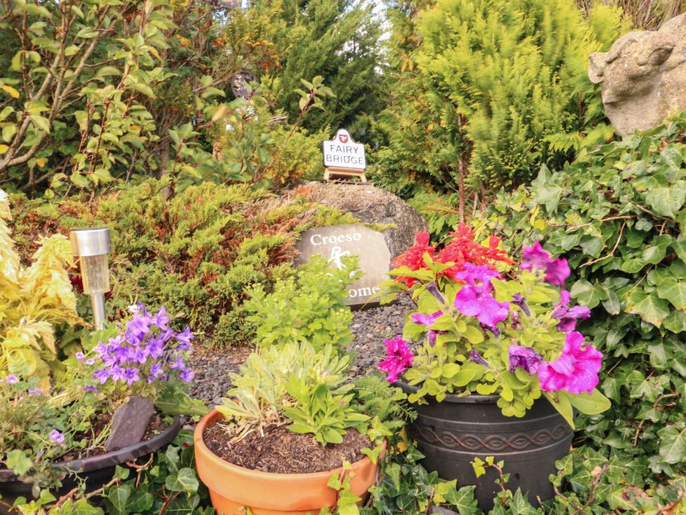 A garden with flowers, a rock, and a sign at Crow's Nest Cottage in Tynygongl near Benllech