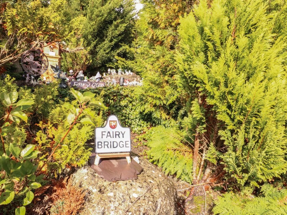 A garden area with a sign for Fairy Bridge and decorative elements at Crow's Nest Cottage Tynygongl near Benllech