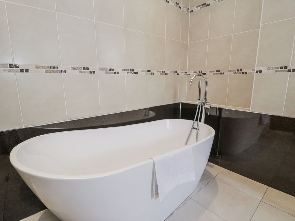 A bathroom with a bathtub and tiled walls at Tyddyn Goronwy in Talybont