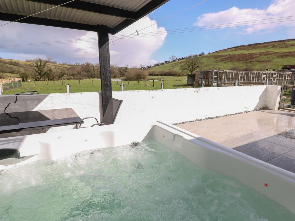 A hot tub and table with view of hills and grass at Meadow View in Laugharne