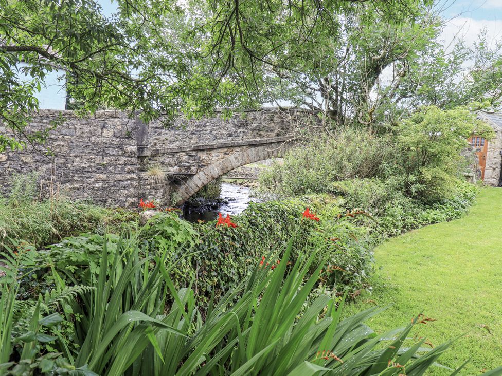 A stone bridge over a stream with plants and flowers at Harber Scar Horton-in-Ribblesdale near Settle