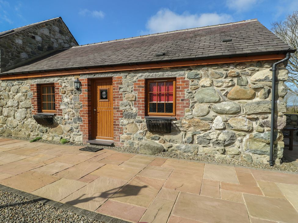 A stone cottage exterior with a wooden door and windows at Poppy Cottage in Caeathro near Caernarfon