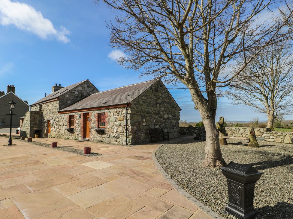 An outdoor area with a stone house and tree at Poppy Cottage in Caeathro near Caernarfon