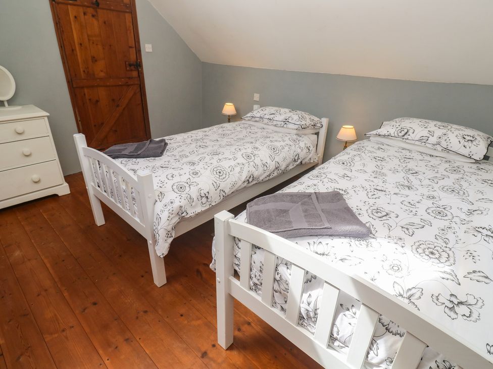 A bedroom with two beds and a wooden door at Longhouse in St Keverne, Lizard Peninsula