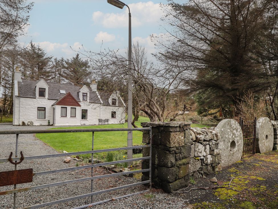 A house and gate with a stone wall and trees at Lag-Uaine in Staffin