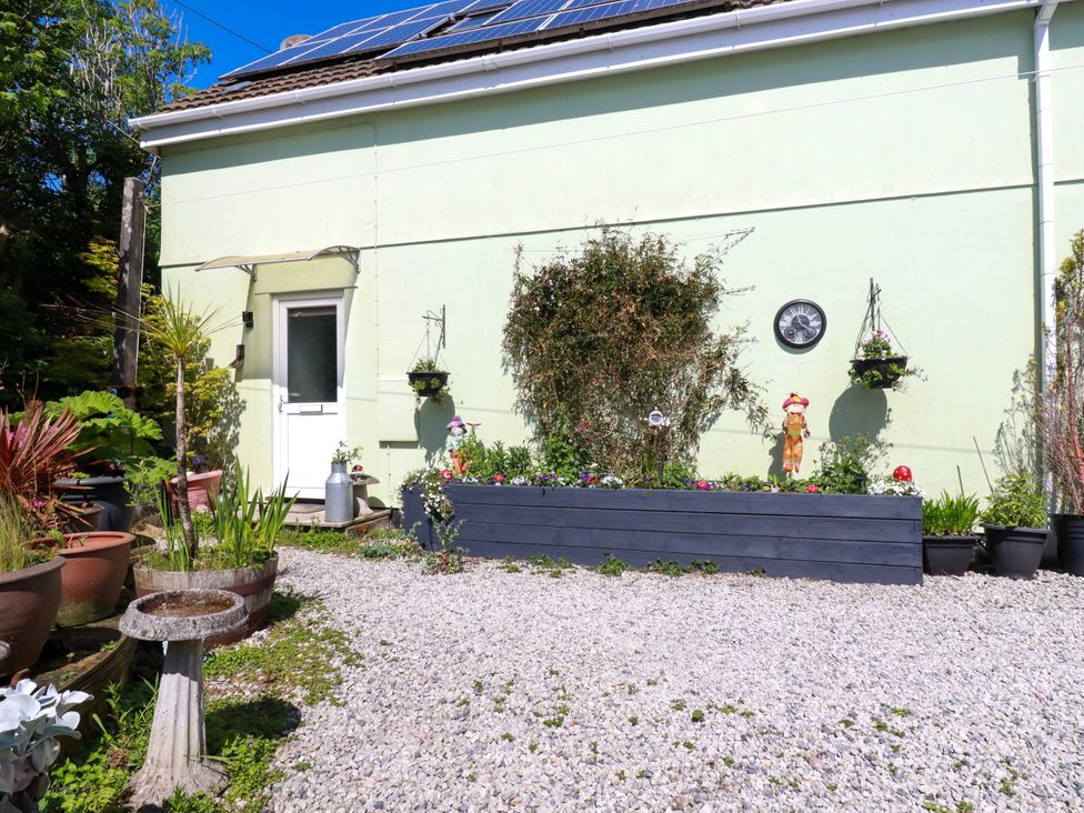 An outdoor garden area with potted plants a gravel ground and a building wall with hanging planters and a clock at Sunnyvale Bugle near St Austell