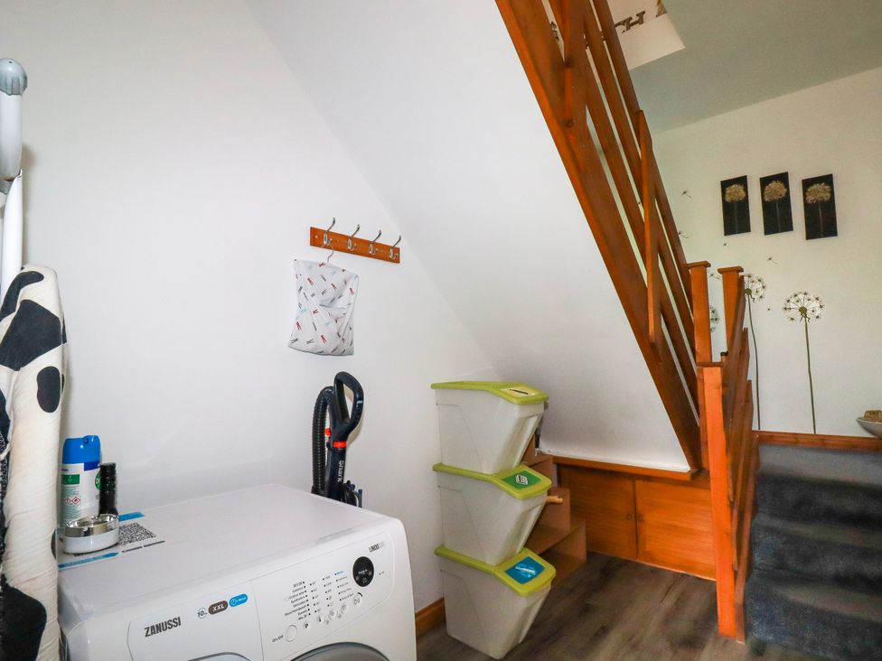 A small utility space with a washing machine stacked bins and wooden stairs with decorations on the wall at Sunnyvale in Bugle near St Austell