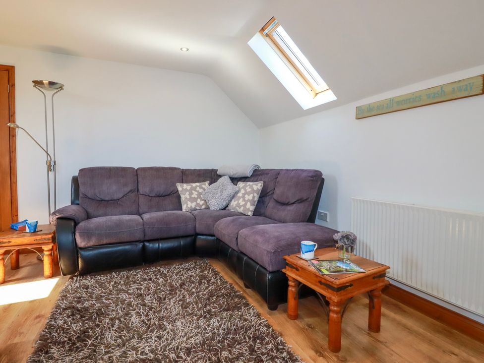 A living room with a purple and black corner sofa a wooden side table with a cup and magazine a floor lamp and a skylight window at Sunnyvale in Bugle near St Austell