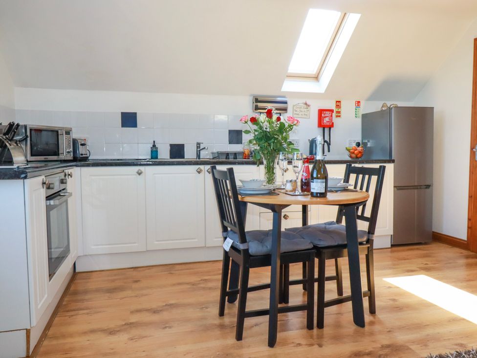 A kitchen with white cabinets a round table with chairs and flowers at Sunnyvale in Bugle near St Austell