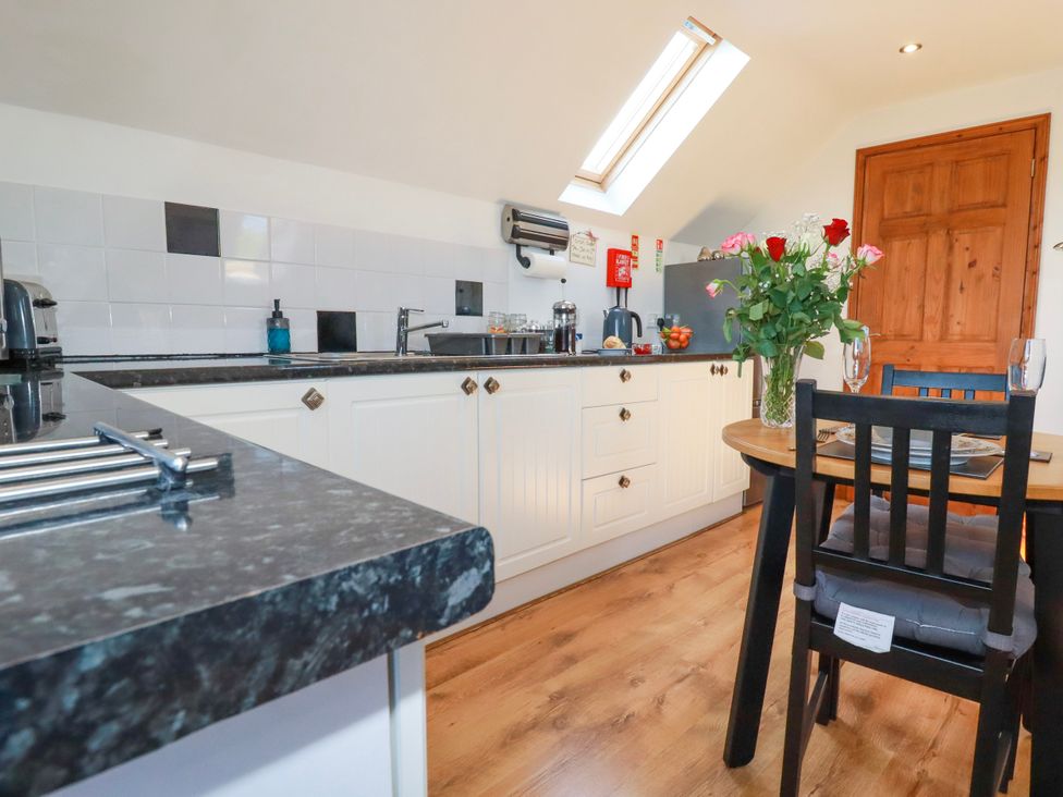 A kitchen with black countertops white cabinets a wooden dining table with chairs and flowers at Sunnyvale in Bugle near St Austell