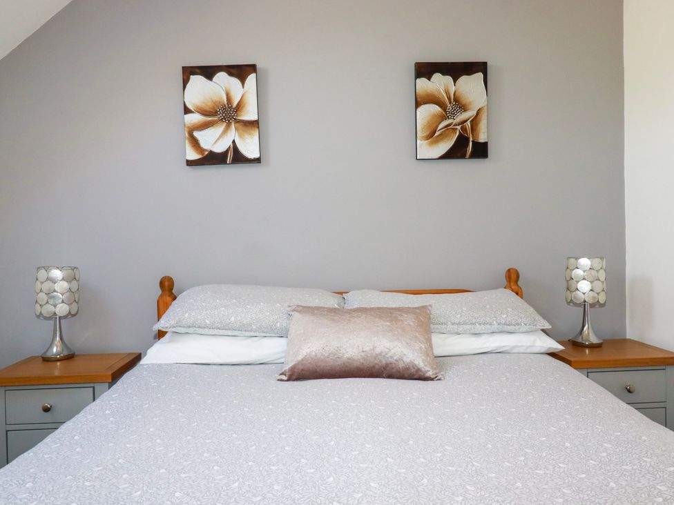 A bedroom with a double bed side tables with lamps and flower paintings on the wall at Sunnyvale in Bugle near St Austell