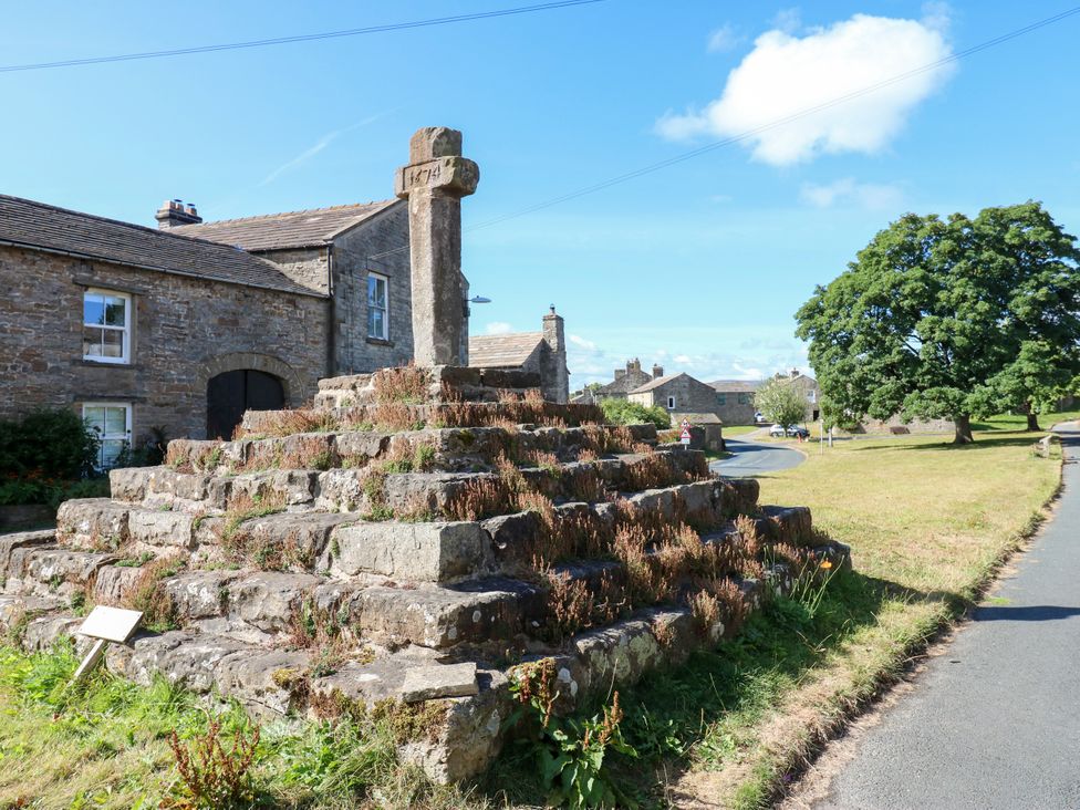 A stone cross on steps with houses nearby at Barnbrook in Carperby near Leyburn