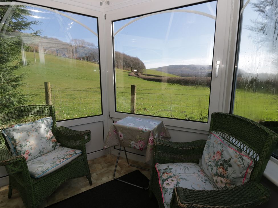 A conservatory with green chairs and a table at Penlone Cottage in Rhayader