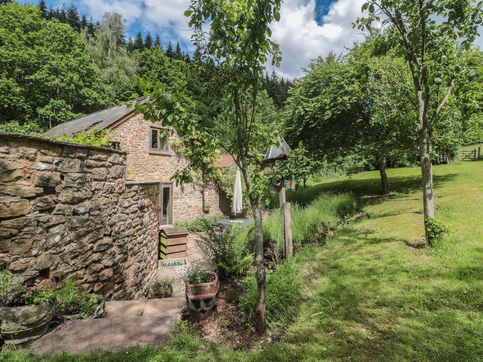 An outdoor view of a stone house surrounded by trees and grass at The Lodge Farm Barn Deepdean near Ross-on-Wye