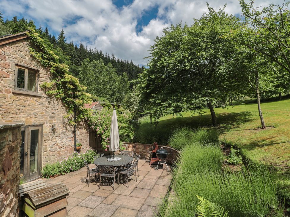 A garden with a stone patio, table, chairs, and trees at The Lodge Farm Barn Deepdean near Ross-on-Wye