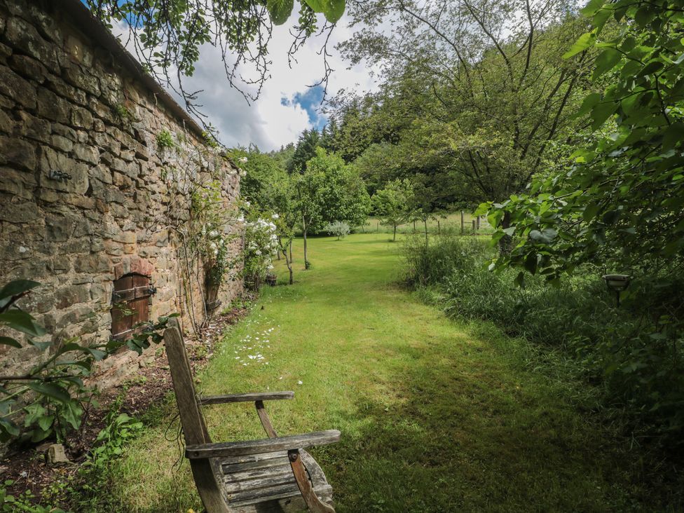 A garden with a stone wall and a wooden chair at The Lodge Farm Barn Deepdean near Ross-on-Wye