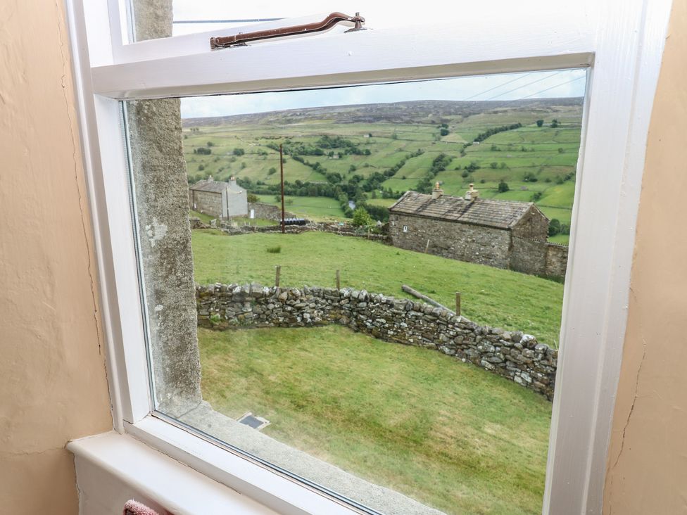 A view from a window showing a landscape with buildings and a stone wall at High Smarber in Low Row near Reeth