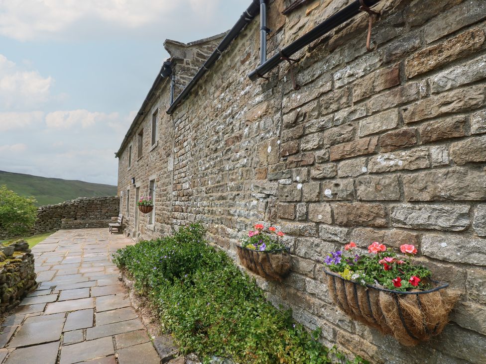 A stone wall with hanging planters and flowers at High Smarber in Low Row near Reeth