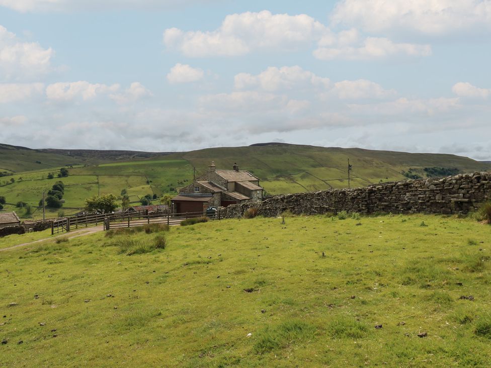 A house with a stone wall and grass field at High Smarber in Low Row near Reeth