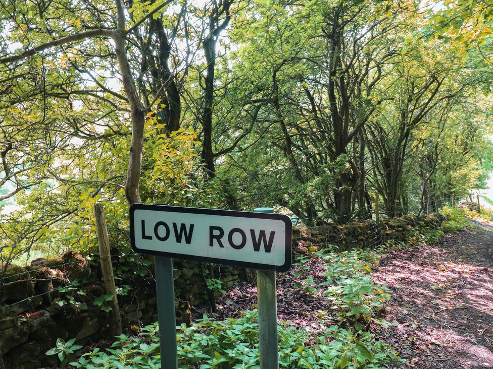 A sign for Low Row surrounded by trees and a path at High Smarber in Low Row near Reeth