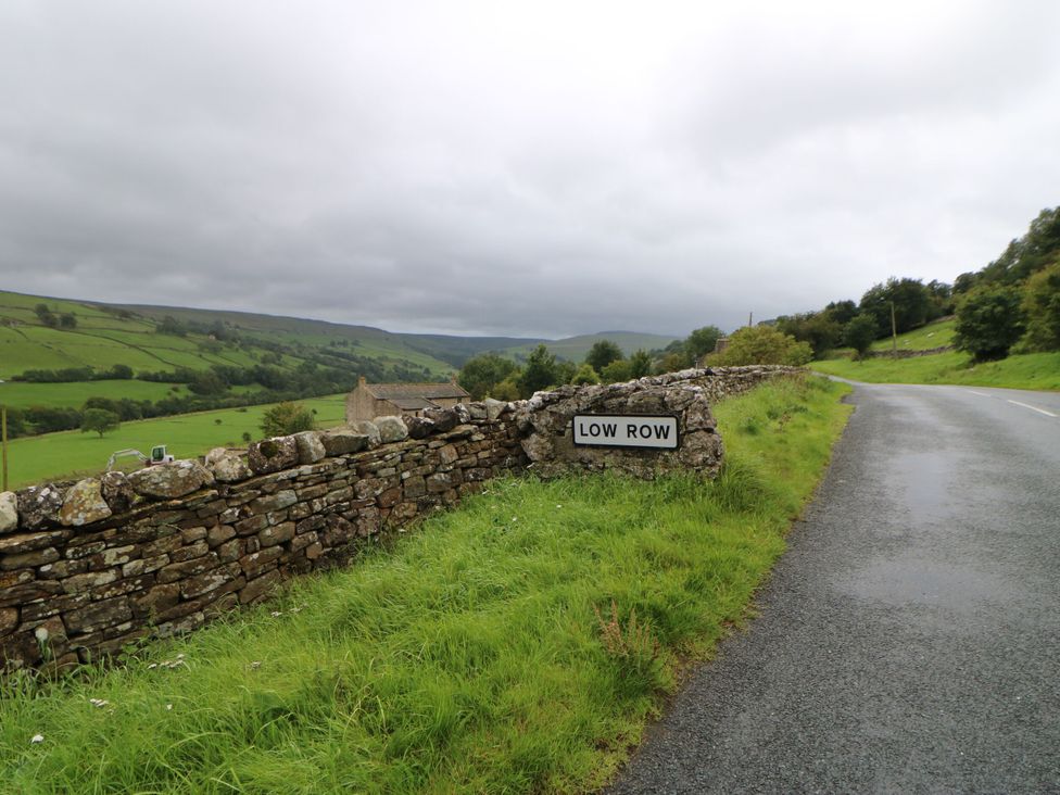 A road sign for Low Row near a stone wall at High Smarber in Low Row near Reeth