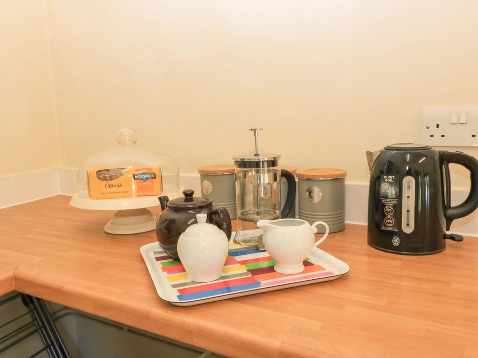 A kitchen countertop with a kettle teapot sugar bowl milk jug French press storage containers and a cake stand with cake at Keepers Cottage in Winterborne Stickland