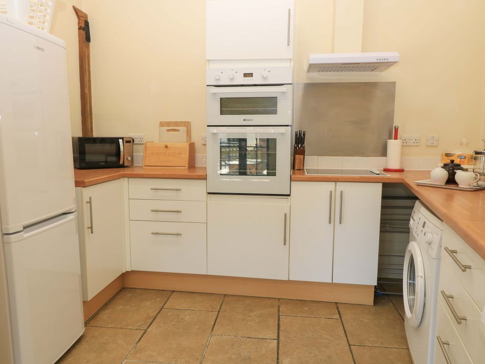 A kitchen with white cabinets a microwave an oven a refrigerator a washing machine and kitchen utensils at Keepers Cottage in Winterborne Stickland
