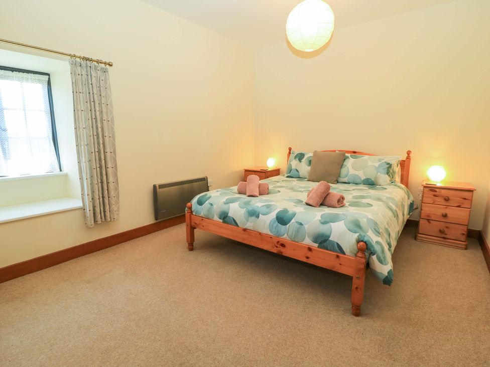A bedroom with a wooden bed with patterned bedding and two bedside tables with lamps at Keepers Cottage in Winterborne Stickland