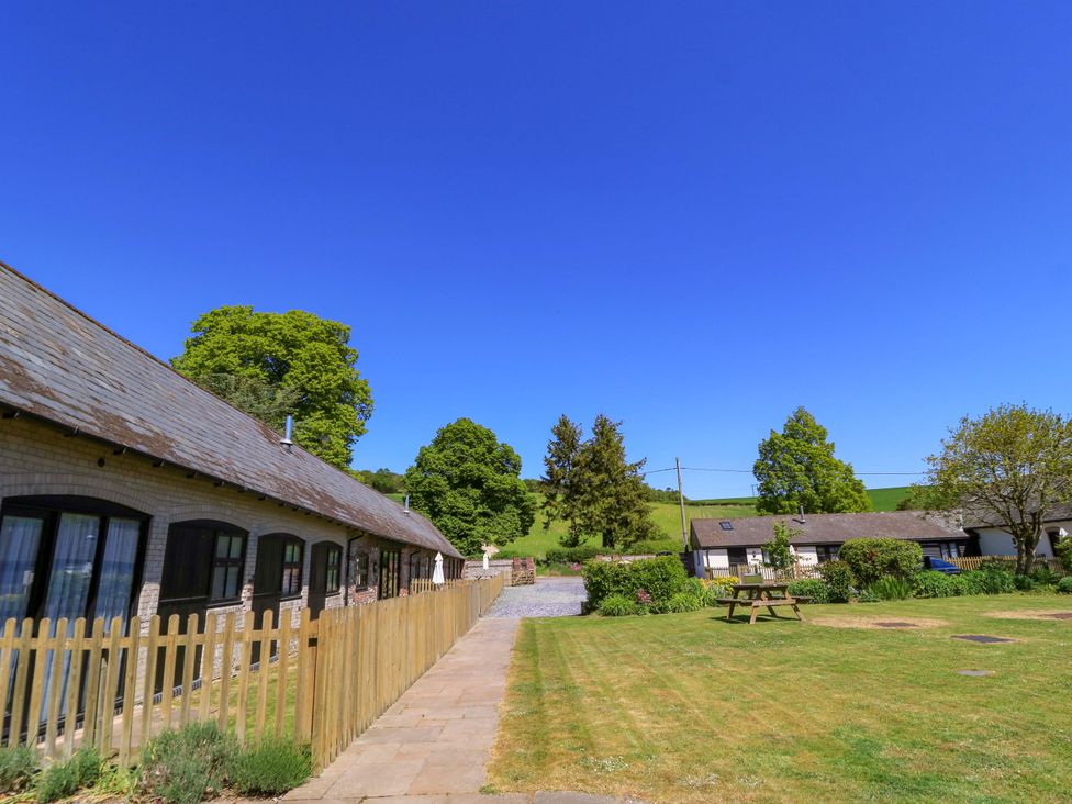 An outdoor area with cottages trees a wooden fence and a picnic table at Keepers Cottage in Winterborne Stickland