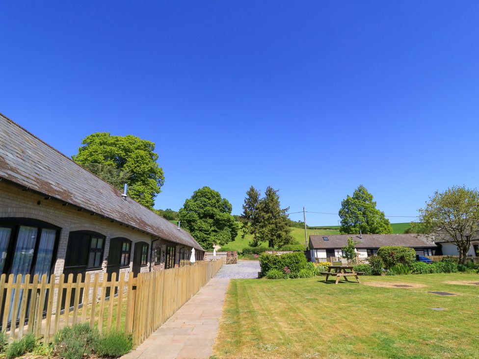 A grassy yard with a picnic table surrounded by buildings and trees at New Barn in Winterborne Stickland