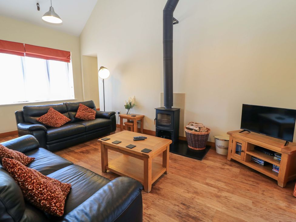 A living room with black leather sofas a wood stove and a television at The Old Cart Shed in Winterborne Stickland