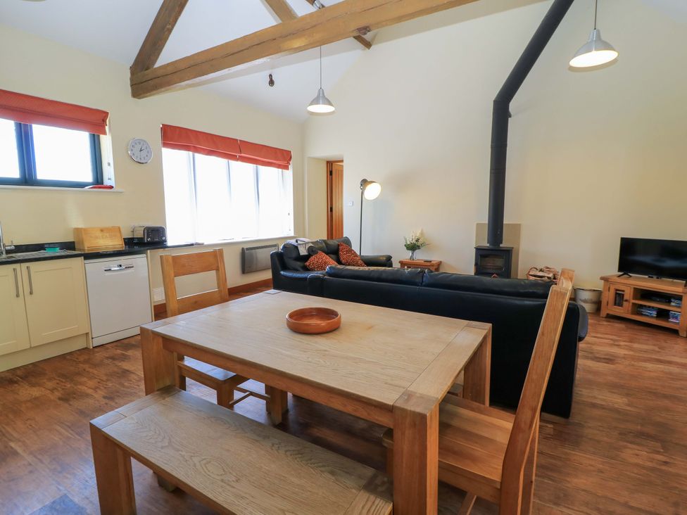 An open plan living area with wooden dining table and bench black sofas wood burner and TV at The Old Cart Shed in Winterborne Stickland
