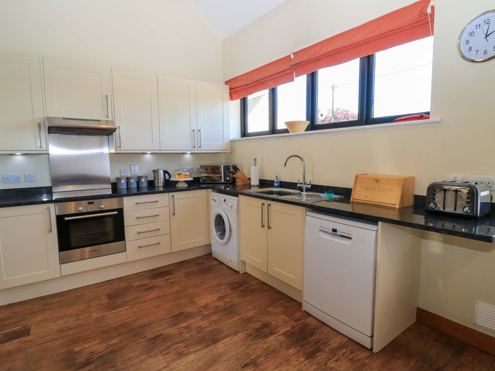 A kitchen with cream cabinets a stainless steel oven washing machine dishwasher and toaster at The Old Cart Shed in Winterborne Stickland