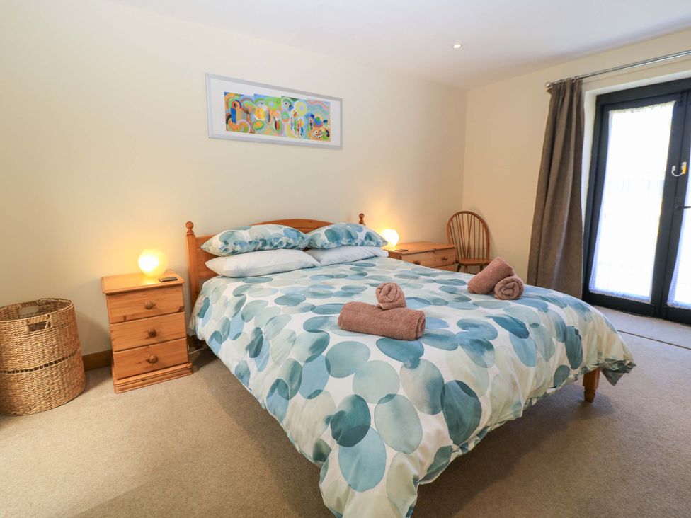 A bedroom with a double bed with patterned bedding bedside tables lamps a chair and a wicker basket at The Old Cart Shed in Winterborne Stickland